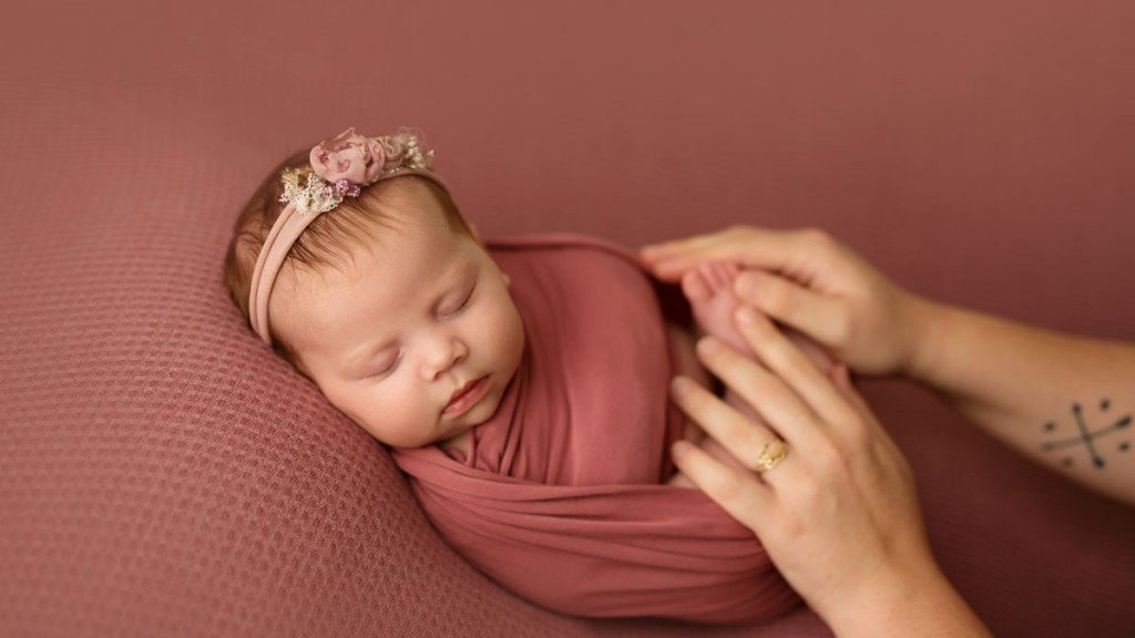 Adding parens hands can add perspective to how small baby is at their newborn photo session. This San Diego newborn sleeps sweetly on a vintage pink backdrop while her newborn photographer poses her gently and includes mom's hands.