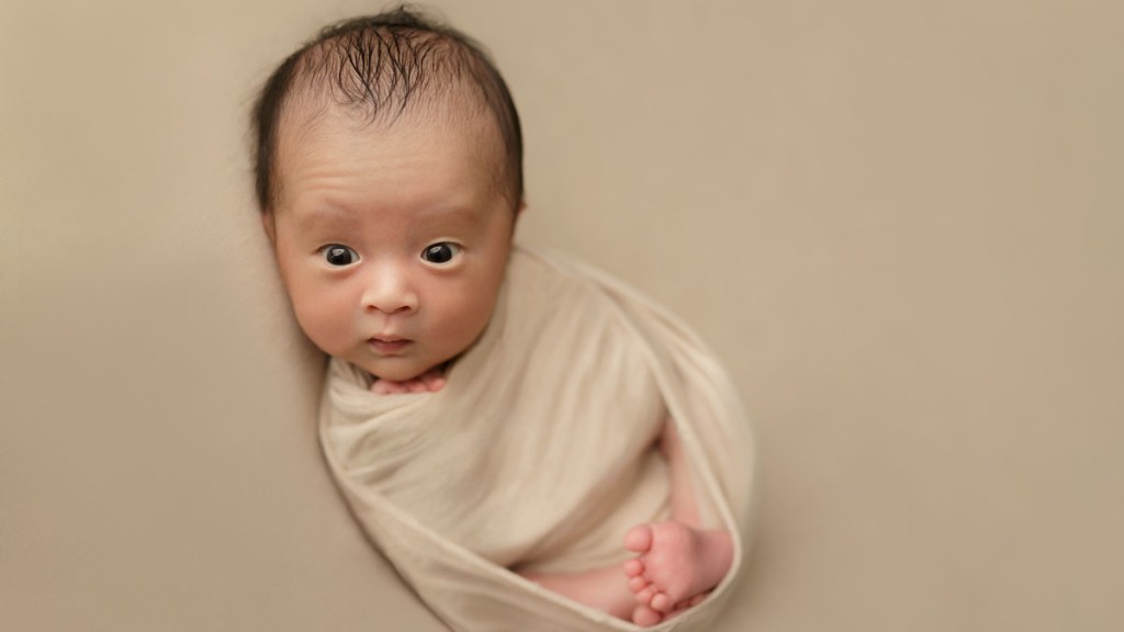 Toes peek out from under baby boy's beige wrap. He is wide awake with eyes open and enjoying his swaddle by Shelly Rosen. Shelly is located in San Marcos, ca, she is a San Diego newborn photographer.