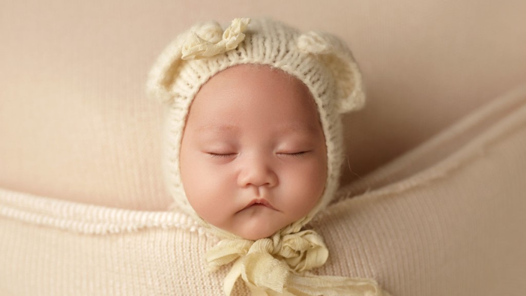 Chubby baby girl cheeks poke out over the covers as this sweet teddy bear sleeps and dreams of her mommy. Image created by Shelly Rosen, San Diego newborn photography.